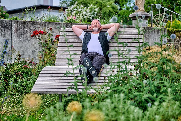 Mann ruht auf Holzliege im Klostergarten Oberelchingen aus Mann ruht auf Holzliege im Klostergarten Oberelchingen aus