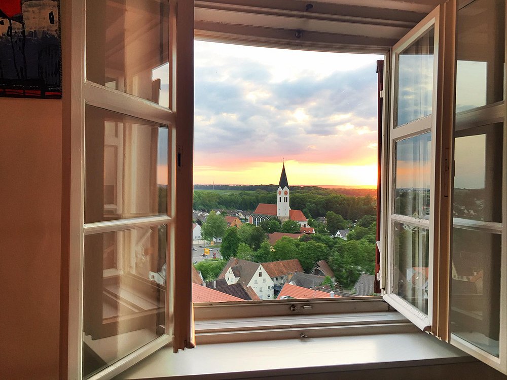 Weit geöffnetes Fenster im 6. Stock des Günzburger Stadtturms mit Blick über die Unterstadt und die St.-Martins-Kirche bis ins Donaumoos. Die untergehende Sonne taucht die Landschaft in warmes Licht Weit geöffnetes Fenster im 6. Stock des Günzburger Stadtturms mit Blick über die Unterstadt und die St.-Martins-Kirche bis ins Donaumoos. Die untergehende Sonne taucht die Landschaft in warmes Licht