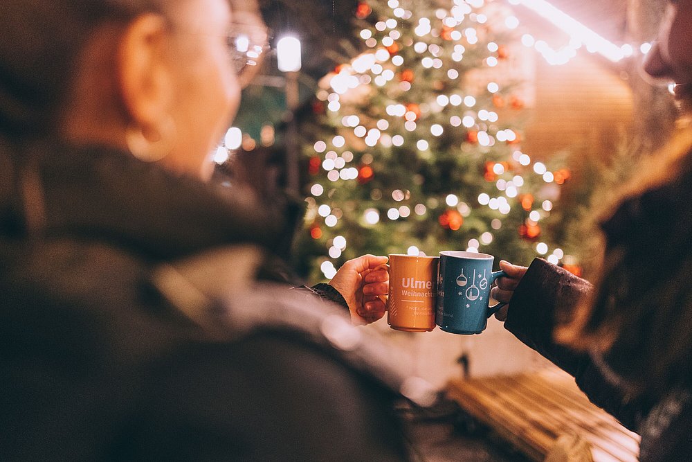 Zwei Personen stoßen mit Glühwein auf dem Weihnachtsmarkt an