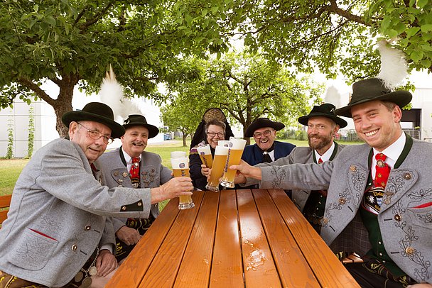 Eine Gruppe Trachtler sitzt unter einen Baum und prostet sich mit Weizenbier zu.