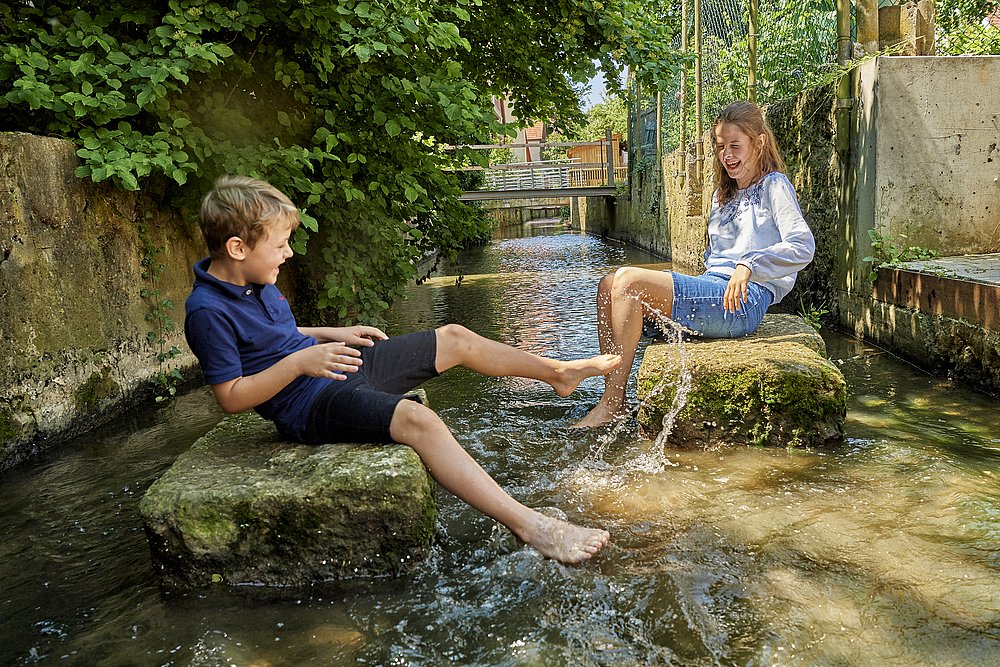 Kinder sitzen auf Steinen beim Kneippbecken im Gerberviertel in Nördlingen 