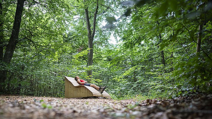 Eine Frau liegt auf einer großen Holzliege mitten im Wald und ruht aus Eine Frau liegt auf einer großen Holzliege mitten im Wald und ruht aus