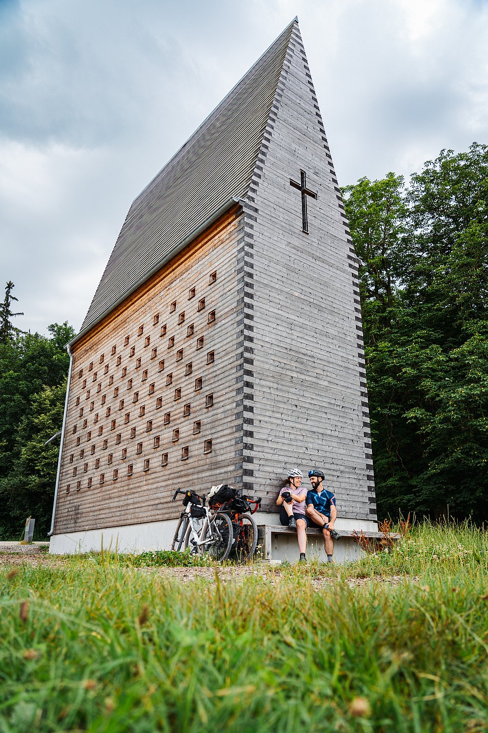 Zwei Fahrradfahrer sitzen entspannt für der Denzel Kapelle von Christoph Mäckler in Oberthürheim Zwei Fahrradfahrer sitzen entspannt für der Denzel Kapelle von Christoph Mäckler in Oberthürheim