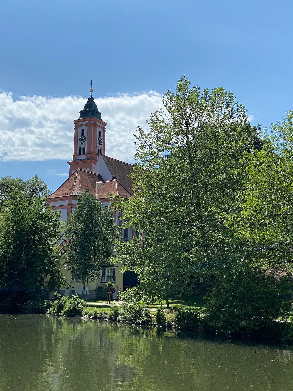 Die Kirche St. Michael in Krumbach vor einer frühlingshaften Wasserkulisse