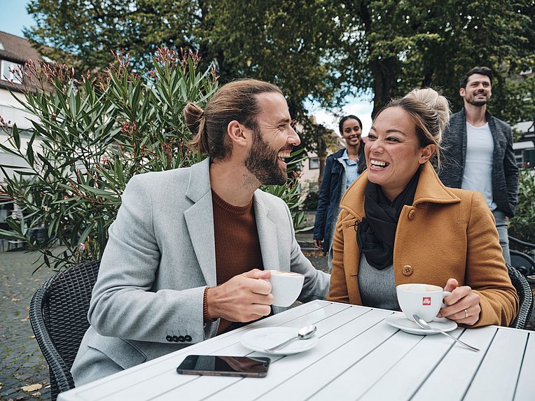 Lächelndes Paar in Mänteln sitzen mit Kaffee in einem Straßencafé Lächelndes Paar in Mänteln sitzen mit Kaffee in einem Straßencafé