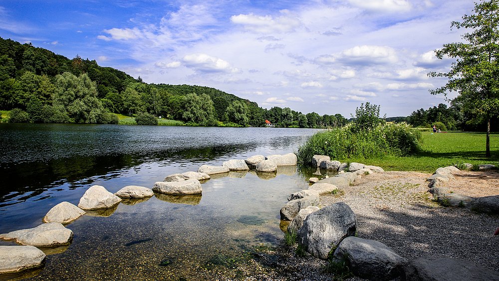See am Wald mit Steinen im Wasser