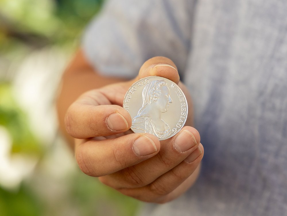 Eine Hand hebt einen Maria-Theresien-Taler Eine Hand hebt einen Maria-Theresien-Taler